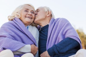 I love you so much! Low angle view of senior man kissing his cheerful wife while being covered with plaid